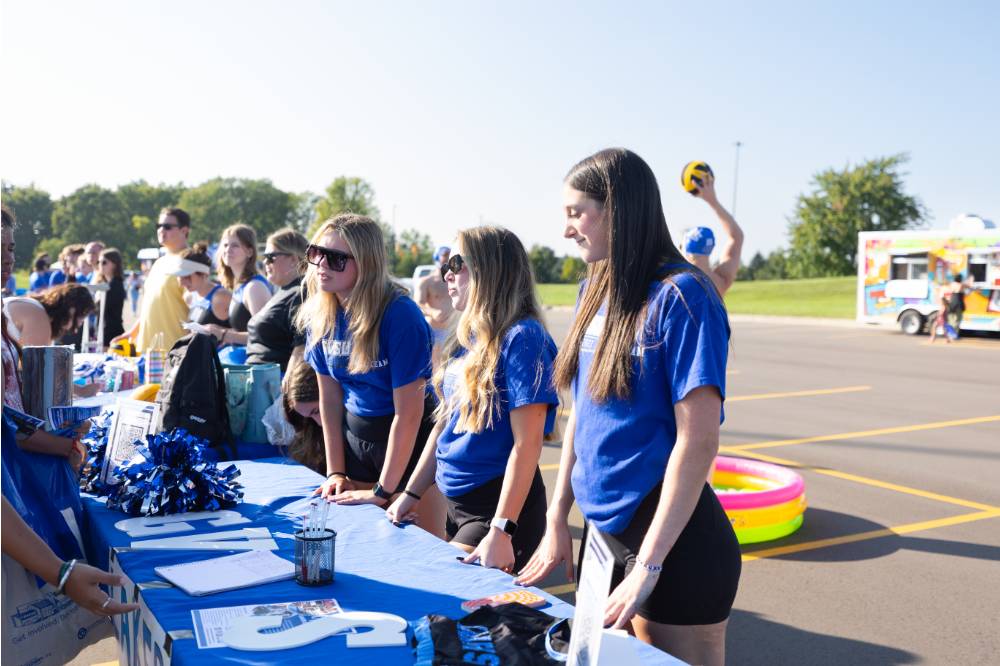 students wearing blue shirts standing at their table during Campus Life Night